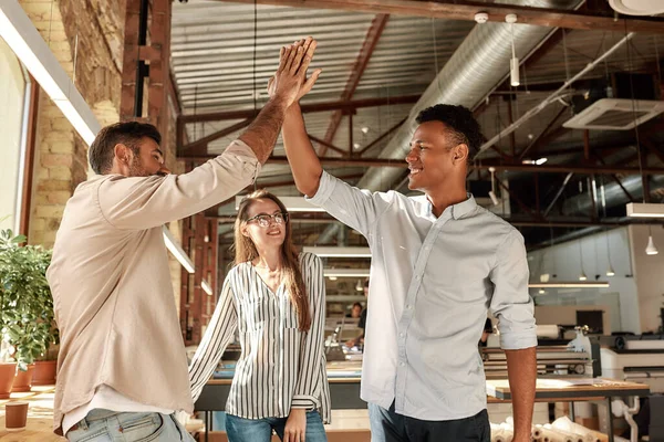 Två glada män ger high-five medan du står med kollegor i det moderna kontoret — Stockfoto