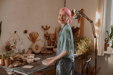 Çömlek atölyesinde duran neşeli bir zanaatkar kadın.