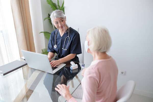 Woman doctor in protective visor talking with patient in her house