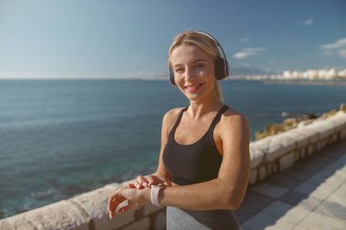 Gülümseyen genç sporcu kadın denizin kenarında ısınma egzersizi yapıyor.