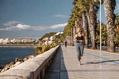 Sportif kadın deniz kıyısında kaldırımda koşuyor.