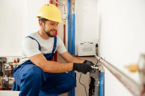 Fröhlicher männlicher Arbeiter, Klempner überprüft Rohre, während er Heizungsanlage in Wohnung installiert — Stockfoto