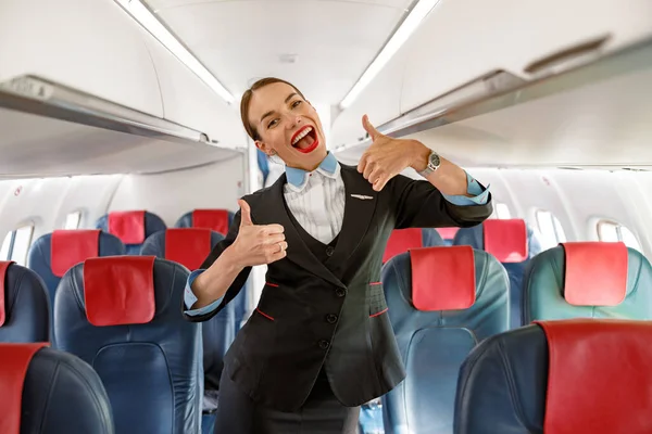 Alegre mujer azafata haciendo pulgares hacia arriba gesto en avión — Foto de Stock