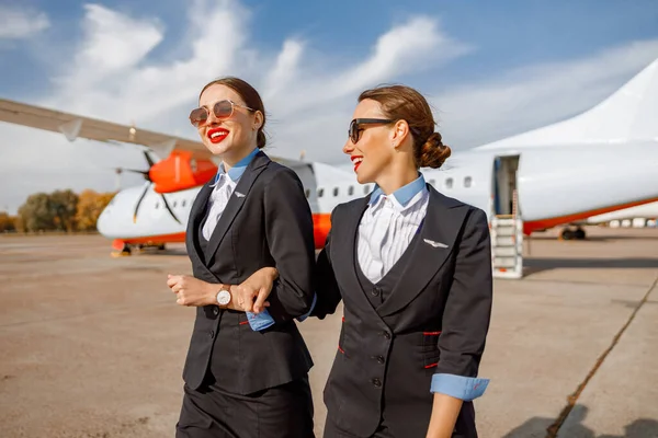 Two cheerful women stewardesses walking down airfield — Stock Photo, Image