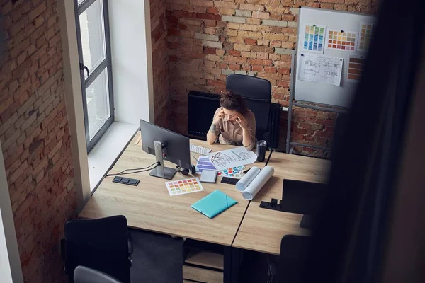 Высокоугольный вид усталой женщины, прикасающейся к своим соблазнам, с натянутой головой во время работы над новым проектом, с использованием компьютера в современном офисе — стоковое фото