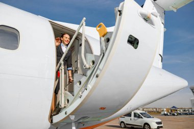 Neşeli bayan hostes, kapanış kapısına bakıyor ve özel uçak jetinde dururken gülümsüyor.