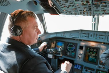 Pilot kulaklık takan bir adam kokpitteki uçakları kontrol ederken cihaz paneli, ekran ve navigasyon sistemleri kullanıyor.