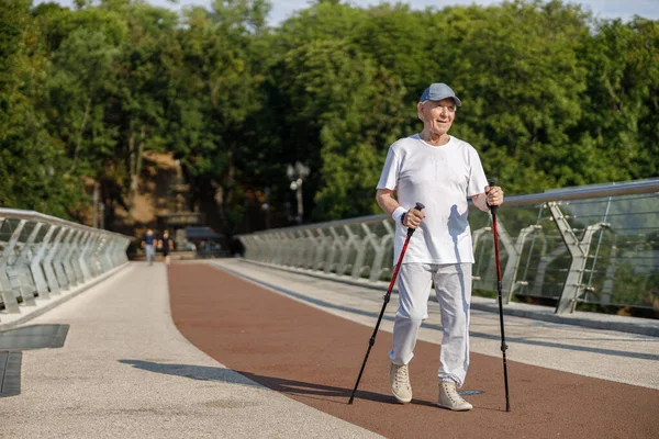 Esportista sênior pratica treinamento de caminhada nórdica em passarela vazia — Fotografia de Stock