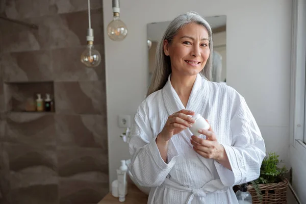 Mooie aziatische vrouw holding cosmetische pot in de badkamer — Stockfoto