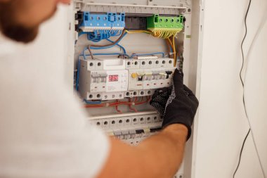 Elektrik teknisyeninin eli, sigortalarla birlikte duvardaki sigorta kontrol dolabında çalışıyor.