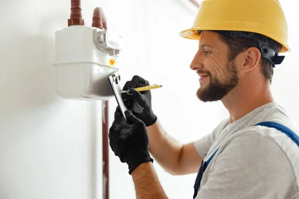 Happy professional heating fitter membuat catatan sambil memeriksa konsumsi gas di pipa gas dan meteran counter — Stok Foto