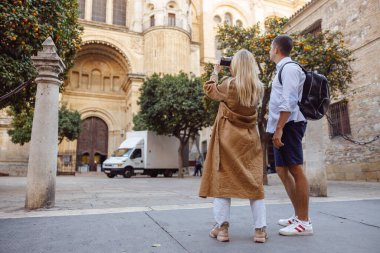 Erkek ve kadın turistlerin yürürken binaların fotoğrafını çekerken çekilmiş uzun bir fotoğraf.