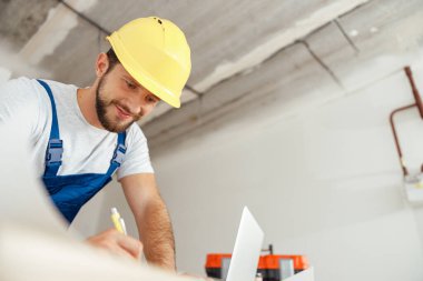 Neşeli tamirci, tadilat sırasında evin içinde beklerken bir emrin detaylarını yazıyor.