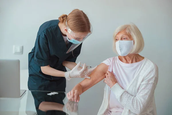 Sjuksköterska ger injektion till äldre kvinna i vardagsrummet — Stockfoto