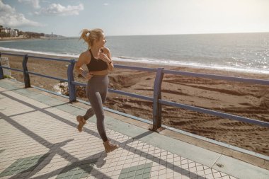 Genç sporcu kadın deniz kenarında tek başına koşuyor.
