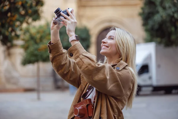 Atractiva mujer sosteniendo cámara retro mientras está de pie en la calle — Foto de Stock
