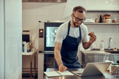 Elinde pasta tutan ve defterinde yazan neşeli bir adam.