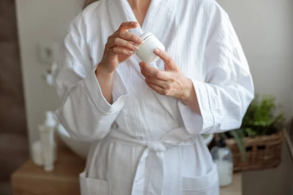 Mujer asiática sosteniendo suavemente frasco cosmético mientras está de pie en la habitación moderna, —  Fotos de Stock