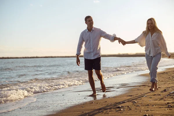 Tampan memegang tangan pacarnya saat berjalan di sepanjang pantai — Stok Foto