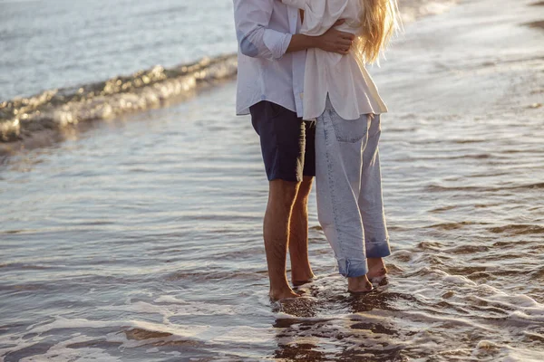 Hombre y mujer abrazándose mientras están de pie con sus pies en el agua en la playa — Foto de Stock