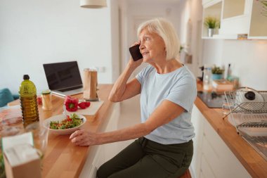 Emekli kadın ev mutfağında iletişim kuruyor.