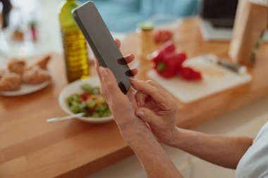 Evde cep telefonu olan yaşlı bir kadının fotoğrafı.