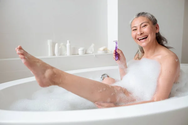 Sorrindo senhora se preparando para remover o cabelo da perna — Fotografia de Stock