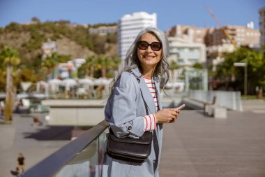 Mutlu Asyalı kadın dışarıda dururken gülümsüyor.