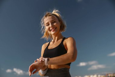 Gülümseyen genç sporcu kadın dışarıda ısınma egzersizi yapıyor.