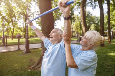Dikkatli bir kadın, kıdemli bir adamın parkta barda egzersiz yapmasına yardım eder.