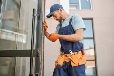 Sakallı genç adam binanın kapısını tamir ediyor.