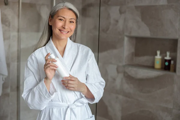 Sorrindo Asiático senhora de pé no banheiro com shampoo — Fotografia de Stock