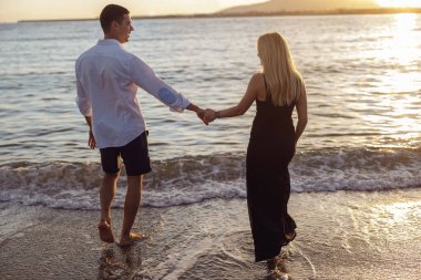 Gün batımında denize doğru yürüyen güzel bir çiftin arka manzarası.