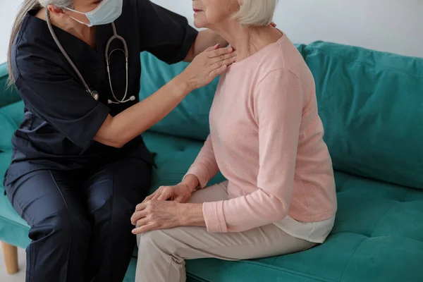 Läkare som vidrör en äldre kvinnas hals — Stockfoto