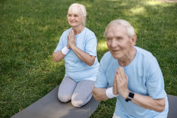 Lächelnde Seniorin mit Ehemann praktiziert Yoga auf Rasenrasen im Park — Stockfoto