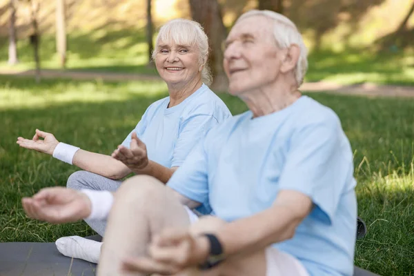 Lächelnde Seniorin sieht entspannten Partner beim gemeinsamen Meditieren im Park — Stockfoto