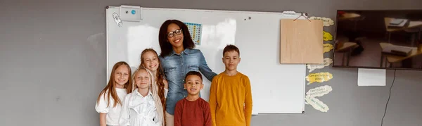 Crianças felizes e um professor posando em sala de aula juntos — Fotografia de Stock