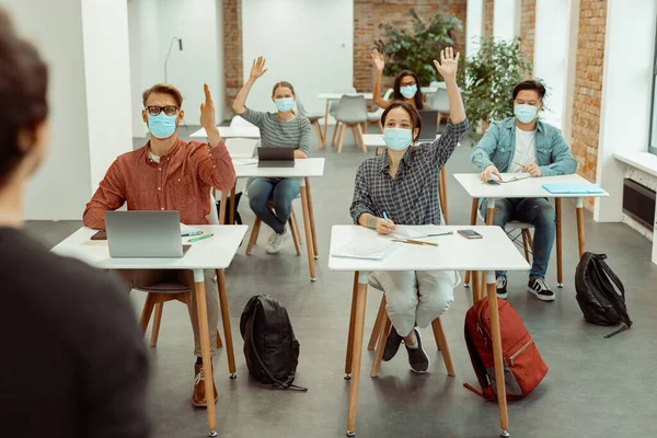 Estudiantes en máscara protectora facial levantando la mano para responder — Foto de Stock