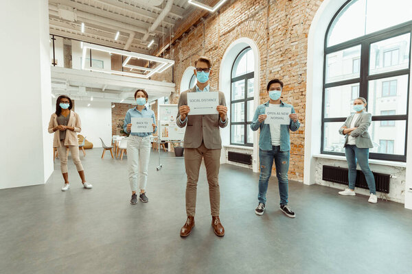 Colleagues in face masks holding sheets of paper with inscriptions