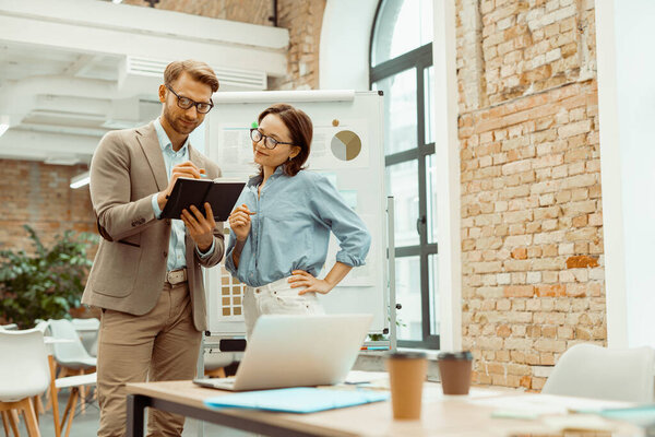 Улыбаясь, двое коллег смотрят на блокнот в офисе