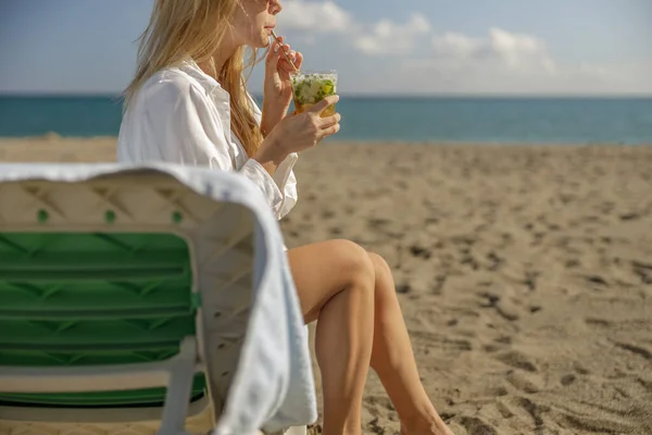 Foto recortada de mujer rubia con cóctel relajante en una tumbona con el mar detrás — Foto de Stock