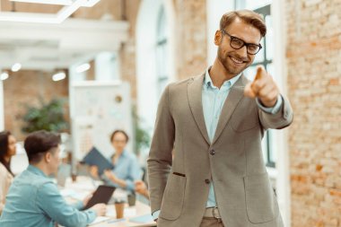 Ofiste duran ve arka planda meslektaşları olan bir adam.