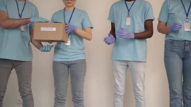 Equipe de diversos jovens voluntários em luvas de proteção passando caixa, trabalhando juntos no projeto de doação dentro de casa — Vídeo de Stock