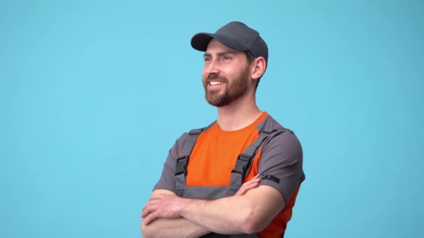 Szállítási alkalmazott ember egyenruhában néz félre, és mosolyog elszigetelt kék háttér — Stock videók