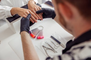 Manikür ustası güzellik merkezinde müşteri çivileri üzerinde çalışıyor.