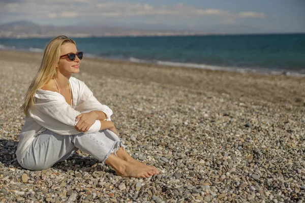 Smiling woman looking away, sitting barefoot on an empty beach during vacation — Foto de Stock