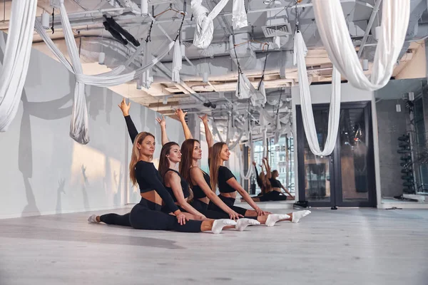Hava yogası eğitiminden önce sicim üzerinde otururken esneme hareketleri yapan bir grup genç kadın.