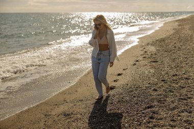 Kaygısız kadın gün batımında deniz kıyısında gezinirken bir telefon görüşmesi yapıyor. Tatil