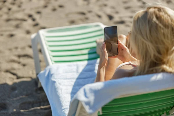 Mujer haciendo videollamadas usando smartphone mientras toma el sol en la playa — Foto de Stock