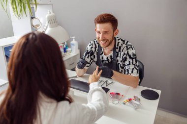 Manikür uzmanı kuaförde müşteriye tırnak hizmeti sunuyor.